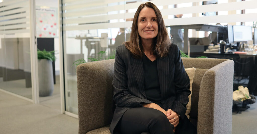 Kvinne sitter i grå stol og smiler til kamera